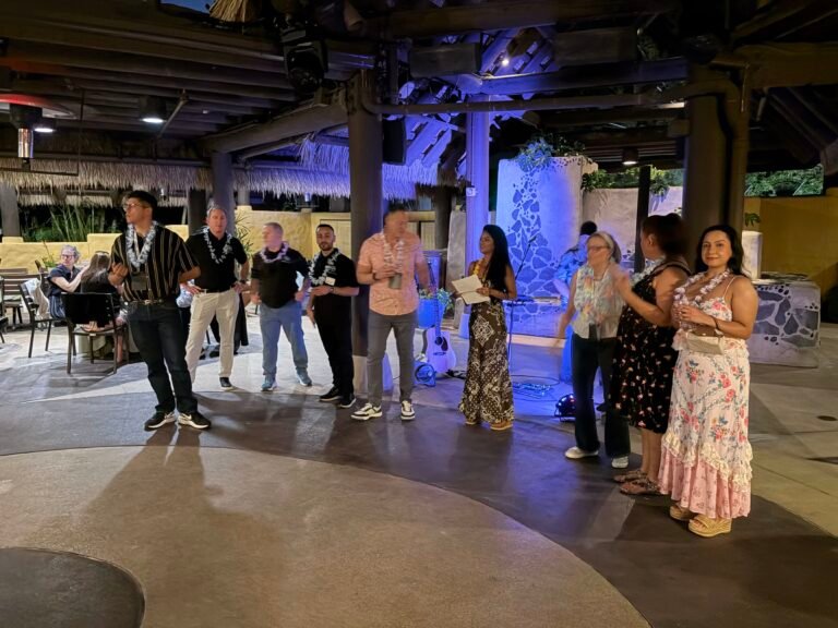 A group of industry professionals gathered beneath a tropical-style pavilion during an evening event with soft blue lighting.