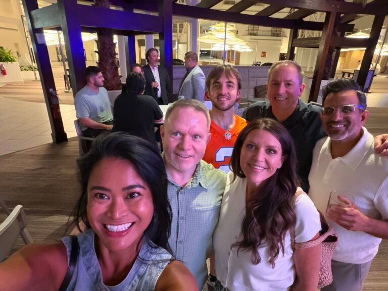 Six smiling adults posing for a group selfie inside a hotel lounge during an evening gathering in Orlando.